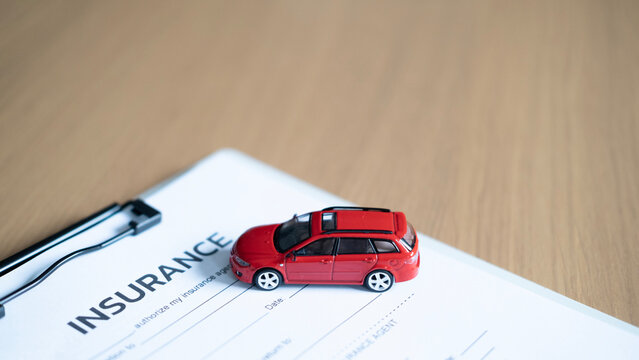 Red model car on auto insurance form and clipboard on wooden desk, representing vehicle insurance, policy, coverage and protection with copy space.