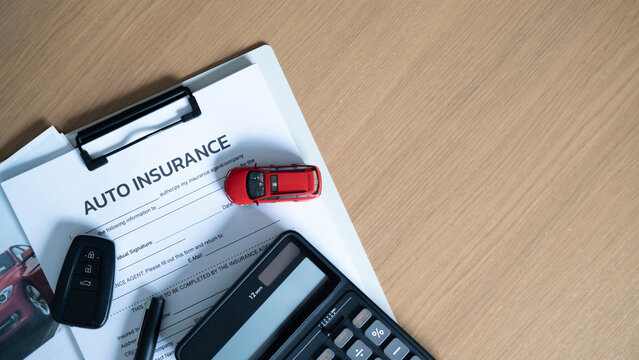 Auto insurance cost and protection concept with red model car, car key, calculator and pen on insurance paperwork with copy space.
