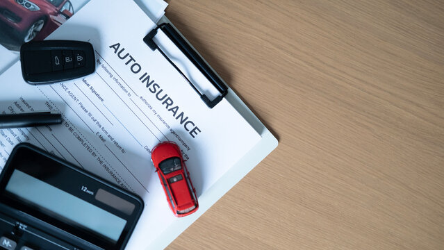 Auto insurance concept with car key, red model car, calculator, pen and insurance form on wooden desk with copy space.