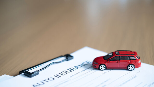 Close-up of red model car on auto insurance document and clipboard, representing vehicle insurance, policy, risk and protection with copy space.