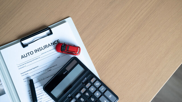 Top view of auto insurance form with red model car, calculator and pen on wooden table with large copy space.