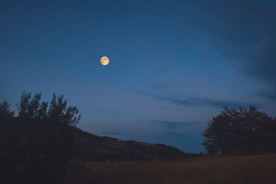 Full Moon, stars and planets above landscape silhouettes in blue hour time.