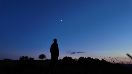 Silhouette of a person in nature observing night sky, Moon, stars and planets from a remote location. © astrosystem