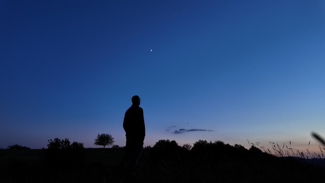 Silhouette of a person in nature observing night sky, Moon, stars and planets from a remote location.