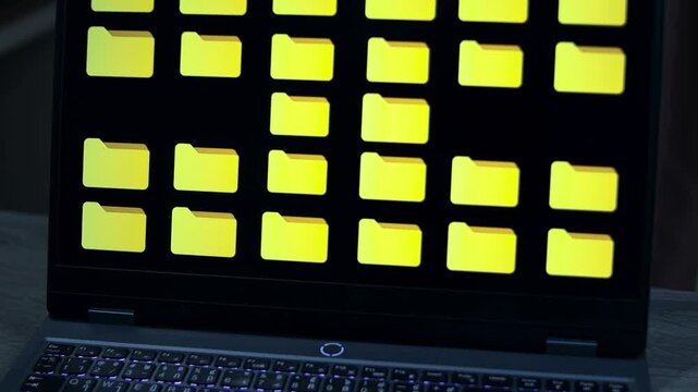 Close-up laptop screen displaying a grid of yellow file folder icons on a dark interface, representing digital file management, data storage, database, document management, and information overload.
