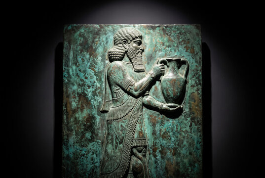 Ancient Assyrian Mesopotamian bronze relief sculpture, carving of a king holding an amphora with green patina.