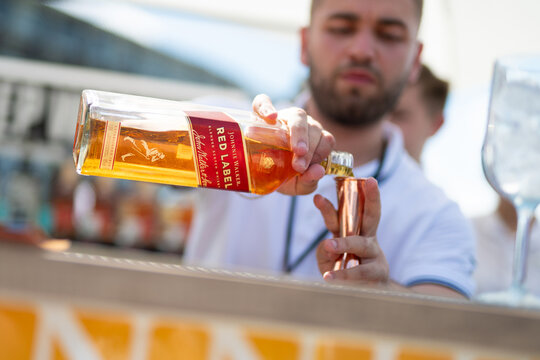 LVIV, UKRAINE - JULY 6, 2024: Close-up of a bartender pouring Johnnie Walker Red Label whisky from a bottle into a copper jigger
