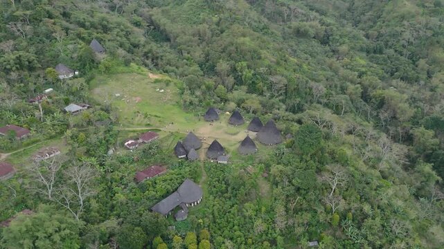 Wae Rebo traditional village on Flores island, an Unesco heritage site, down-looking aerial sunny view over the woody houses with villagers walking around, must-see destination in Indonesia and Asia