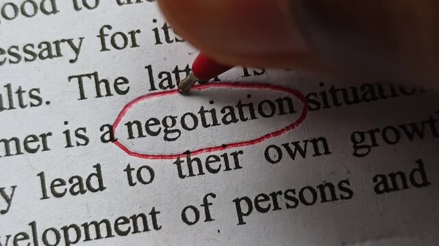 Closeup of hand with red pen mark circle around to emphasize or highlight negotiation word printed on book or magazine paper. Negotiation or rapport business skill importance abstract symbolic concept