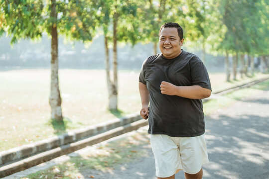 portrait of an overweight Asian man jogging in the park in the morning with copyspace