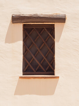 Rustic wooden lattice window with timber lintel in a beige plaster wall