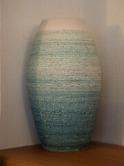 Handmade textured ceramic vase in white and turquoise on a wooden shelf © Inna