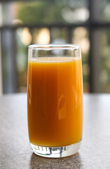 Glass of fresh orange juice standing on a surface with a blurred background. © Ink N Propeller