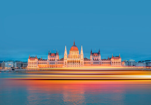 Hungarian parliament in Budapest with motion speed light of passing ferry in the foreground at twilight blue hour    - Budapest, Hungary