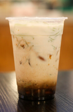 Cold cendol dessert drink with coconut milk, palm sugar syrup, and green rice flour jellies served in a clear plastic cup.