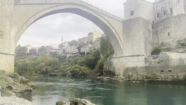 Handheld low angle pan up from Neretva riverbank revealing the historic Mostar Bridge in Bosnia