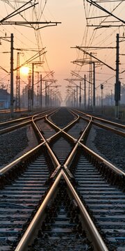 Converging Railway Tracks at Sunrise with Overhead Wires and Misty Horizon