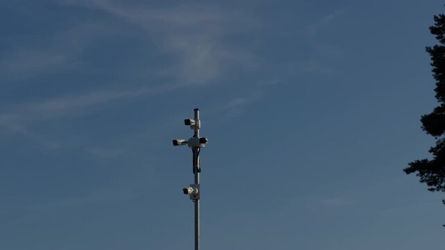 Security camera cluster mounted on tall pole against clear blue sky with tree silhouette