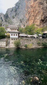 Vertical pan right showcasing flowing river water historic Blagaj Tekke and cave entrance