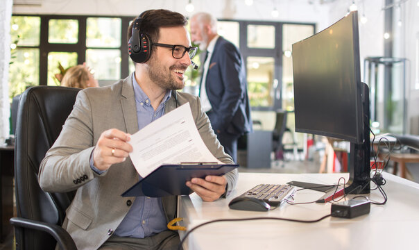Cheerful call center representative checking documents on clipboard while sitting at desk