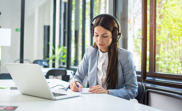 Young call center operator taking notes during customer support phone call