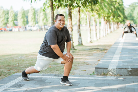 overweight man smiling while stretching thigh muscles before exercising in park