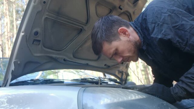 Upset man repairing car engine with ratchet wrench under open hood, struggling with breakdown. Vehicle maintenance, car trouble. Frustrated man repairing car engine with ratchet wrench on roadside