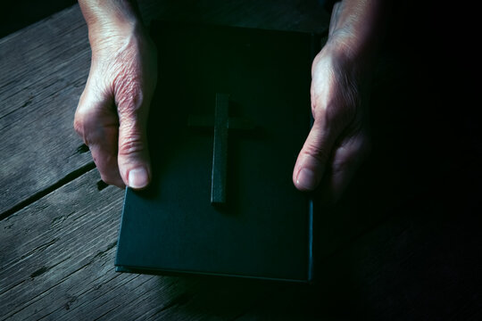 Old woman hands with rosary beads and bible on wooden background