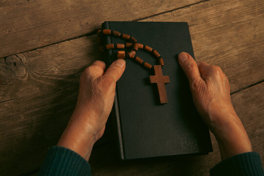 Old woman hands with rosary beads and bible on wooden background
