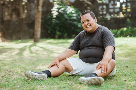 Asian fat man smiling in sportswear sitting down in an outdoor background