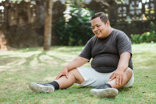 Asian fat man wearing sportswear sits leisurely below while in an outdoor background