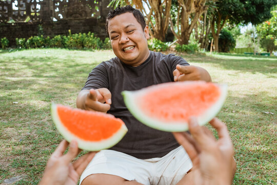 fat man with accepting gesture when offered watermelon in outdoor background