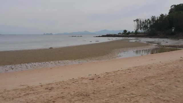 A peaceful and overcast summer afternoon overlooking the low tide shoreline at Bang Makham Beach in Koh Samui, Thailand