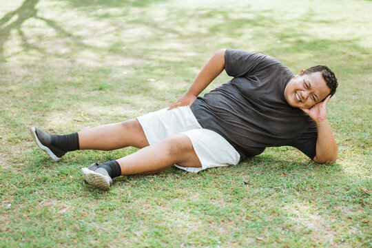 fat man wearing workout clothes lays back and relaxes in an outdoor background