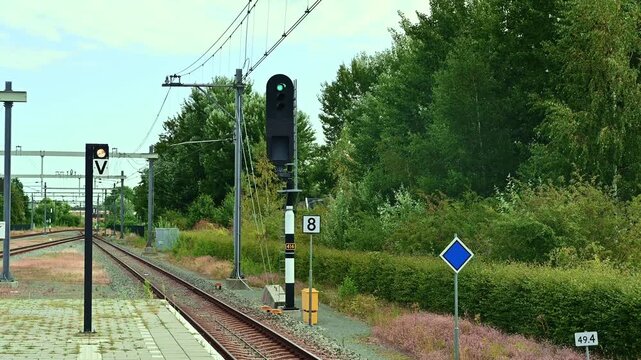 Railway signals along the tracks in Netherlands, showing a green main signal and a white signal with letter V. Train transportation, signaling system, Dutch railway infrastructure.