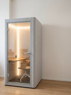 Modern soundproof office pod with warm LED lighting, desk, and chair, designed for private work in a minimalist room.
