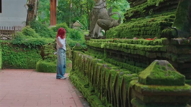 Woman praying at moss covered Wat Phra Lat temple in Chiang Mai Thailand, Female worshipping to sacred statue at peaceful Buddhist shrine by ancient tropical architecture 4k