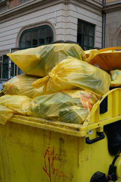 Yellow bins with yellow plastic waste bags ready for collection in an urban area vertical.