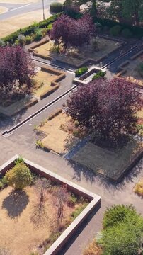 Aston Hall drought-stricken gardens filmed from a drone in a diagonal flyover, revealing ornate formal layout, dry lawns, clipped hedges, and historic estate grounds in summer heat. Vertical format.