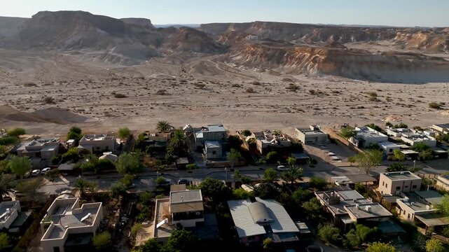 4K 60fps drone footage hovering above Zukim, Israel, rotating clockwise to reveal a sweeping panoramic view of the entire village, surrounding desert, cliffs and Arava landscape