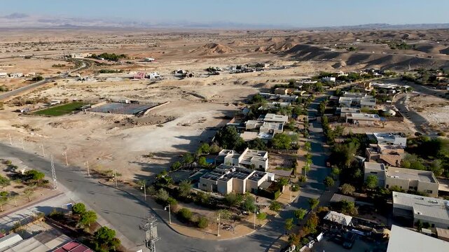 4K 60fps drone footage hovering above Zukim, Israel, rotating clockwise to reveal a sweeping panoramic view of the entire village, surrounding desert, cliffs and Arava landscape