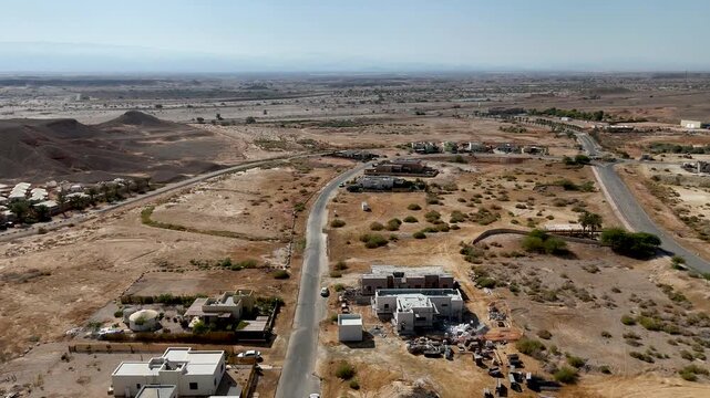 4K 60fps drone footage flying backward from Zukim, Israel, moving westward over the village toward the remote desert, revealing homes, rugged terrain, cliffs and expansive Arava scenery
