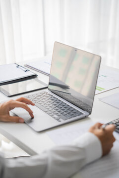 Asian businessman writing on document and typing on laptop
