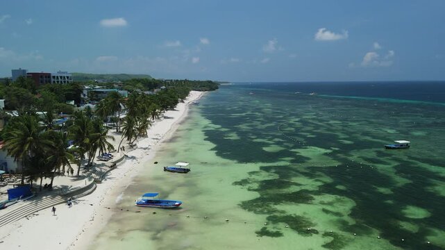 Drone descends while flying over Alona Beach, showing white sand, shallow reef water, boats, palms, and coastline in Panglao, Bohol