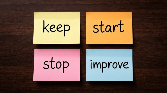 Colorful sticky notes with keep, start, stop, and improve words on a wooden desk.
