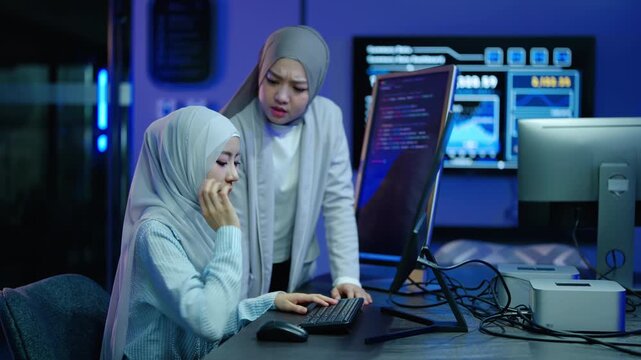 Angry Muslim female manager in hijab scolding stressed programmer employee at computer desk in modern dark office. Toxic workplace environment, demanding boss criticizing frustrated coder worker.