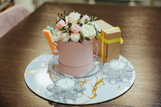 Elegant floral candle arrangement in a pink round box displayed with wrapped gift boxes and white tealight candles on a reflective decorative tray