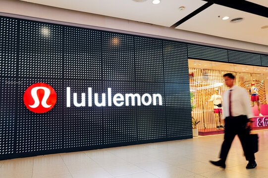 Modern storefront of lululemon athletic apparel store with red logo sign and motion blur pedestrian walking past in shopping mall