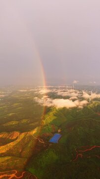 Vertical Video: Double rainbow over spinning wind turbines with low-lying sea of clouds drifting over green hills in sunshower