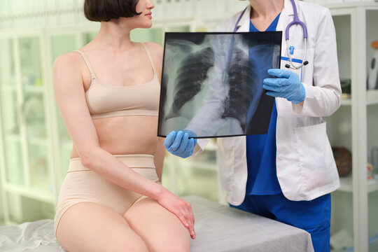 A doctor is closely examining an X-ray image with a patient in a clinic or hospital setting. The scene captures a professional and clinical interaction, highlighting the use of a medical st.